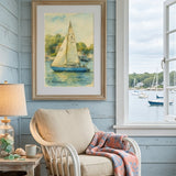 A framed sailboat painting hangs on a light blue wood-paneled wall above a white wicker armchair with a pink patterned throw blanket. A window to the right shows water and boats outside, and a side table with a lamp and books sits to the left.