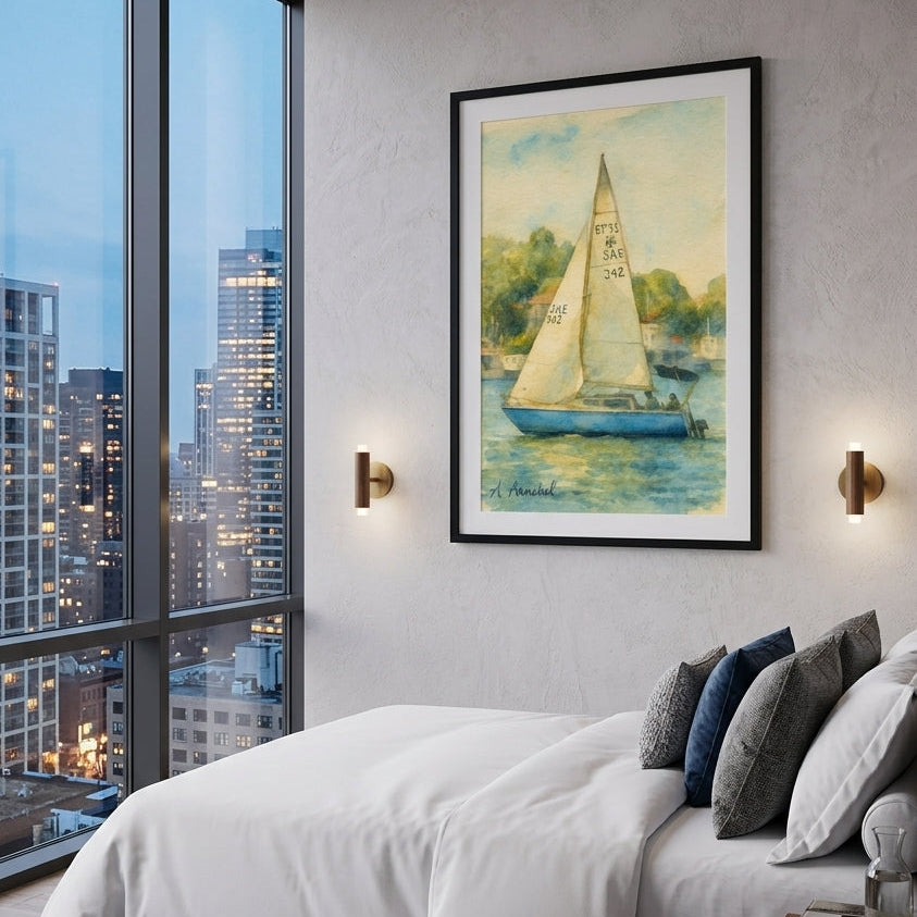 A framed art print of a sailboat on water, hung on a gray wall in a modern bedroom setting with a bed, pillows, and a large window showing a city skyline at dusk.