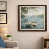 A framed landscape painting of a calm lake with a small rowboat and a dock, displayed on a beige wall in a styled living room setting next to a sofa, lamp, and bookshelf.