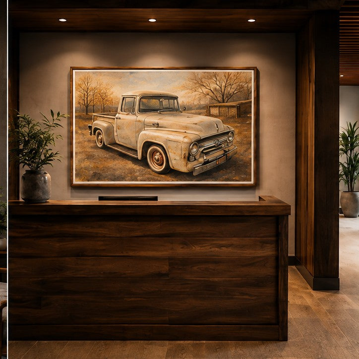 A large framed wall art print depicting a vintage pickup truck in a warm-toned outdoor scene, displayed above a dark wood reception desk in a modern interior setting.