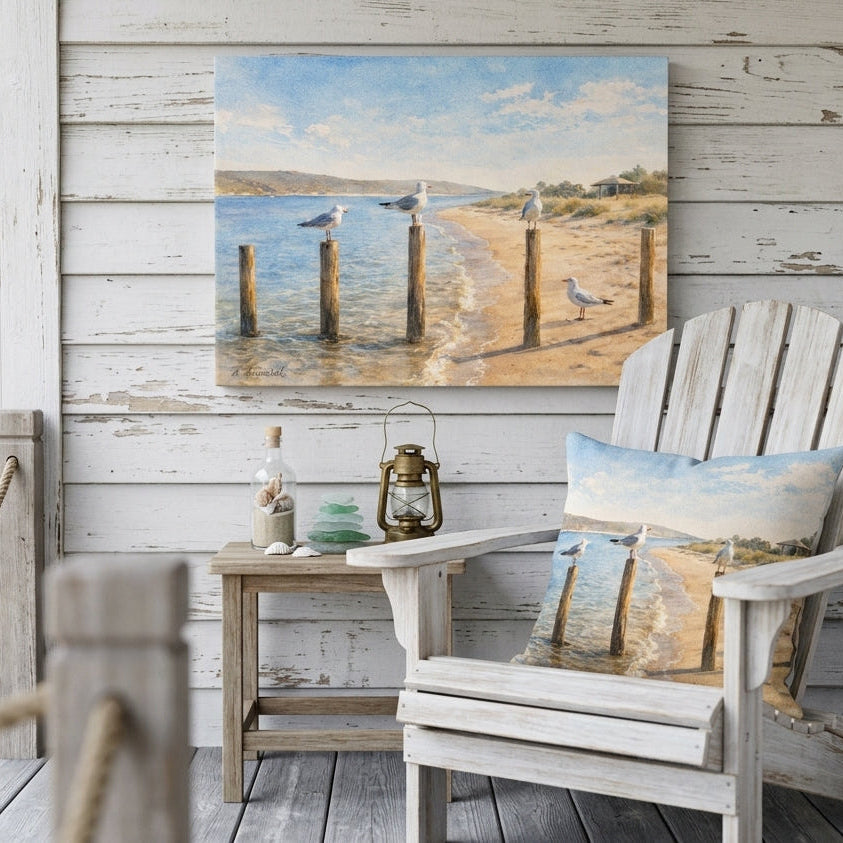A coastal beach scene canvas print hangs on a white wood porch wall above a white Adirondack chair with a matching pillow, alongside a small wooden side table with decorative items.