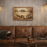 A framed vintage pickup truck painting hangs on a corrugated metal wall above a brown leather couch in a rustic room setting with two hanging lamps, a helmet, and a small table with a bottle and glass.